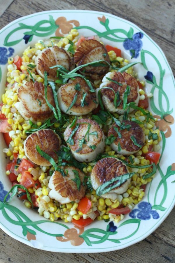 Scallops on a platter on a bed of corn and tomatoes and basil