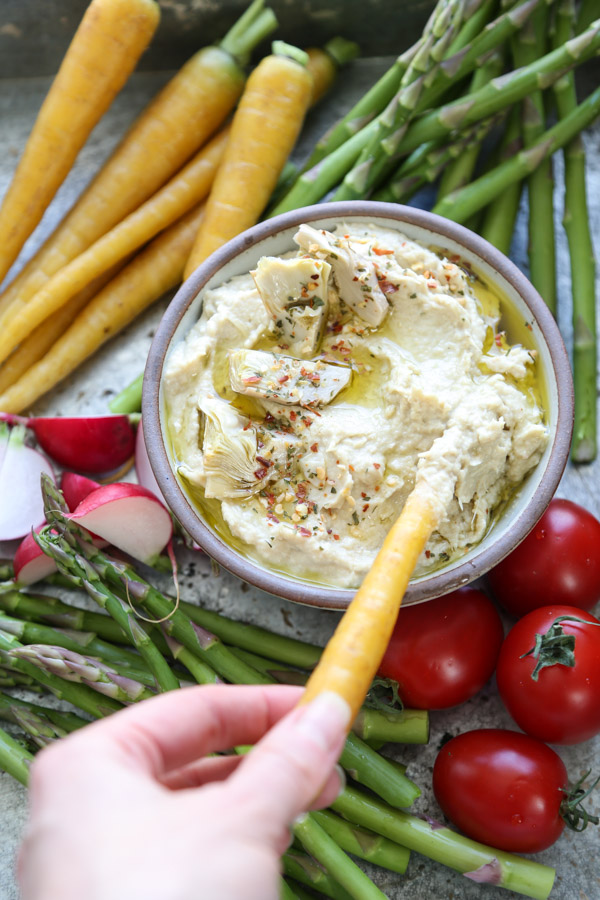 bowl of hummus with crudites on a tray hand dipping