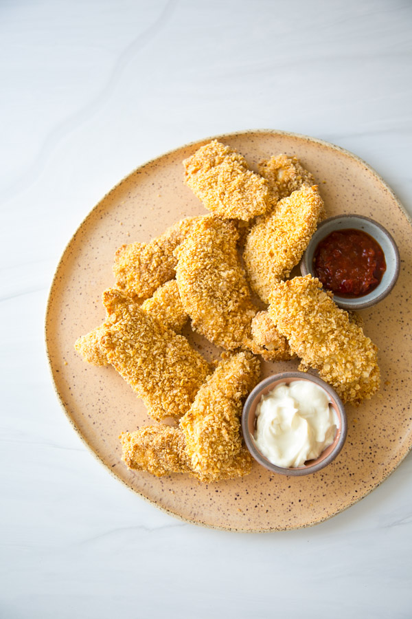 crispy baked gluten-free chicken strips on a platter with ketchup and mayo dipping bowls