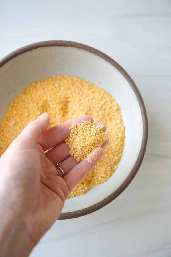 gluten-free cornflake coating in a bowl with hands holding a tablespoon