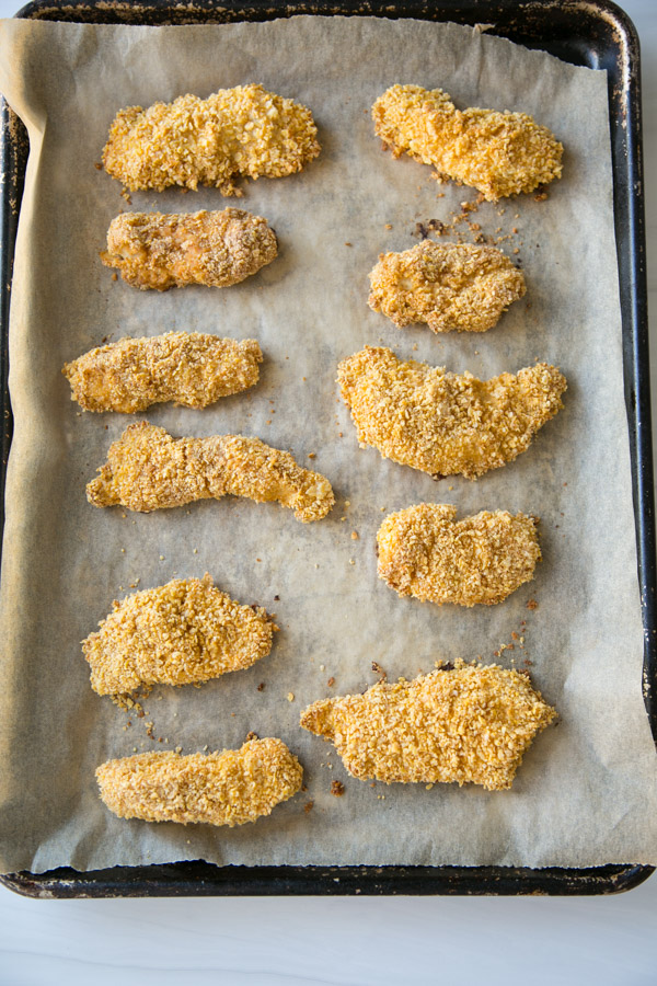 crispy baked gluten-free chicken strips coated in cornflakes on a sheet pan