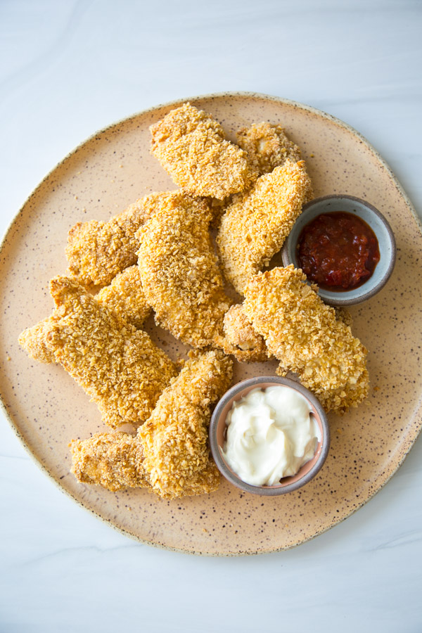 crispy baked gluten-free chicken tenders on a platter with ketchup and mayo dipping bowls