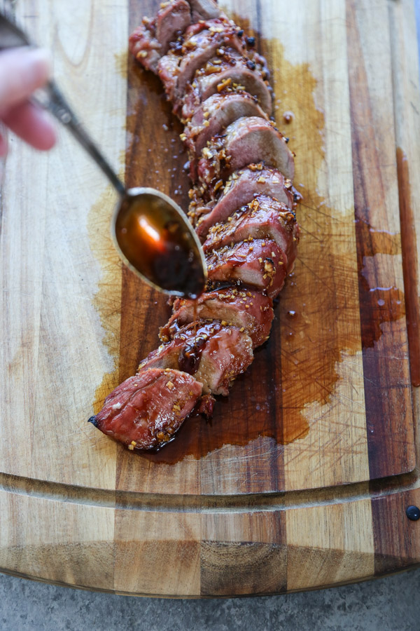 sheet pan Teriyaki Pork Tenderloin on a cutting board with marinade and spoon