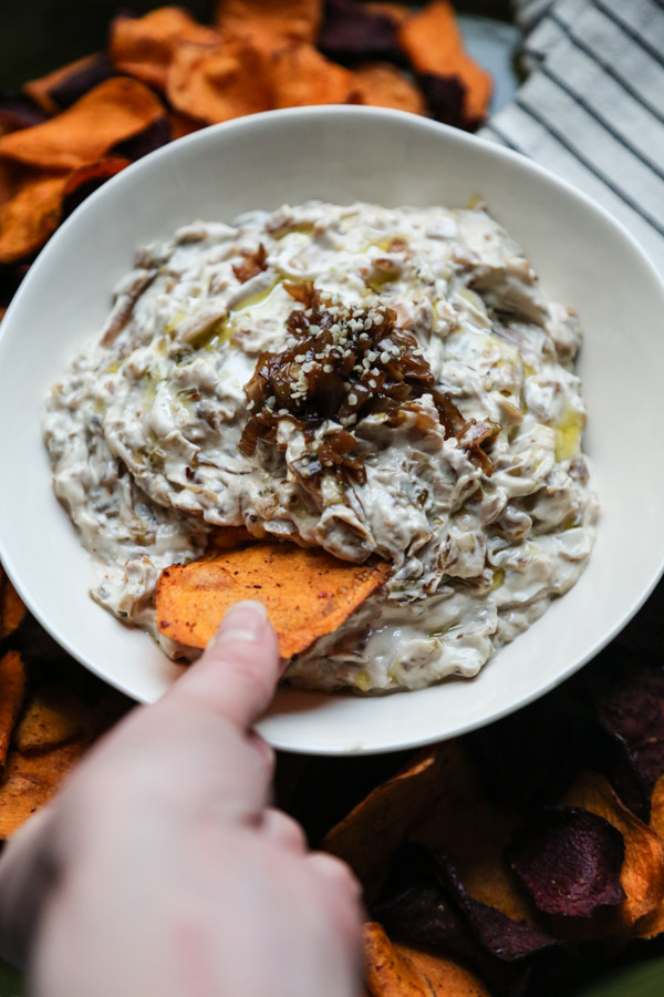 hand dipping sweet potato chip into bowl of gluten-free french onion dip
