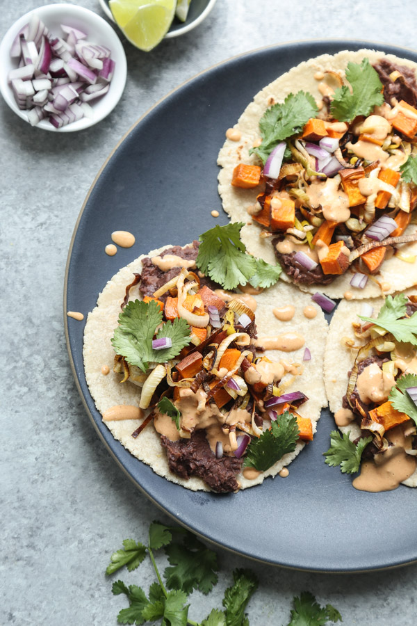 These vegetarian black bean tacos are made with chile-spiked refried beans, roasted sweet potato- leek hash, and spicy chipotle tahini sauce. Easy + delish! | Feed Me Phoebe