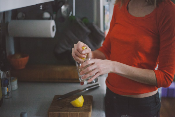 Phoebe Lapine the author squeezing lemon juice into a glass in the kitchen