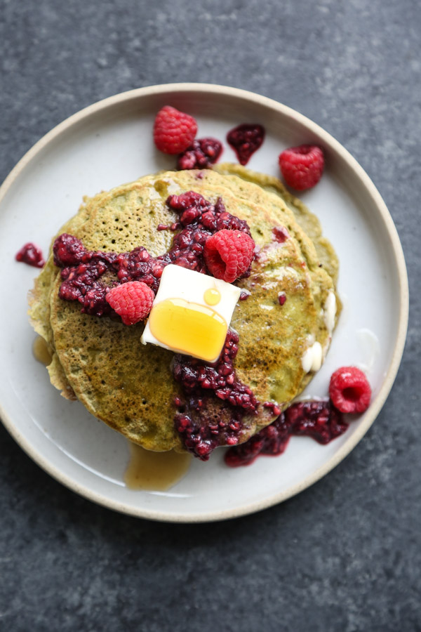 stack of green pancakes with raspberries on a plate