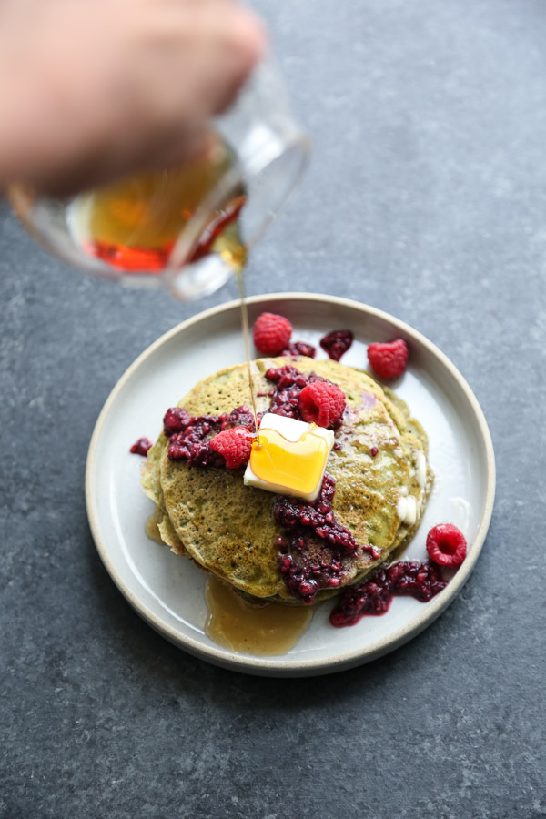 stack of green pancakes with raspberries on a plate