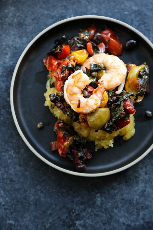 A bowl full of shrimp, cherry tomatoes, chard, puttanesca sauce.