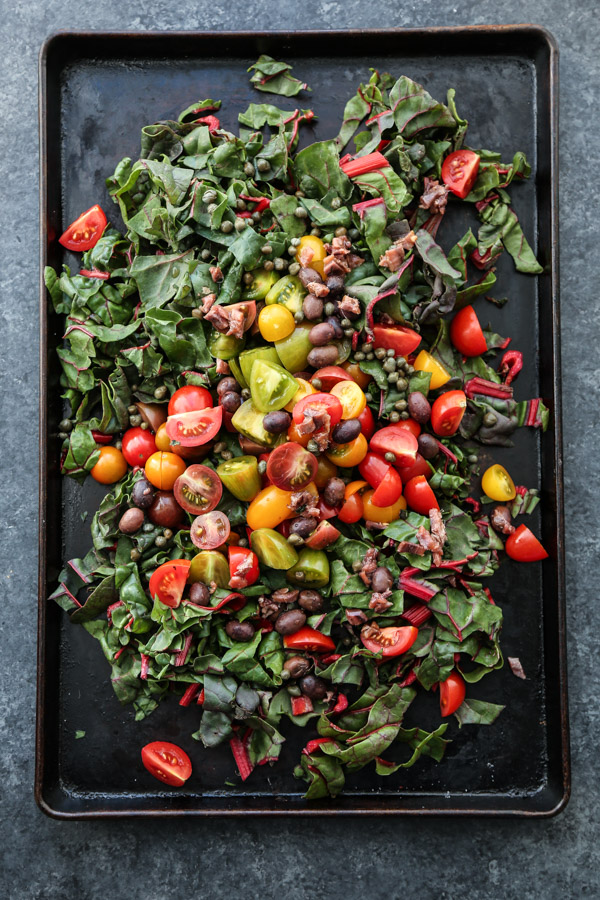 A sheet pan full of cherry tomatoes, olives, chard, puttanesca sauce.