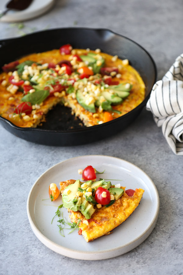 Mexican Frittata with Avocado, Corn and Tomatoes in a Skillet on a table with plate