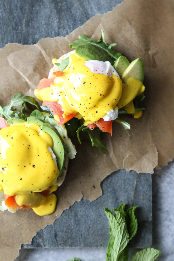 English muffin with salmon and avocado on a serving tray with herbs, eggs hollandaise and salmon