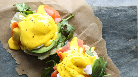 English muffin with salmon and avocado on a serving tray with herbs, eggs hollandaise and salmon