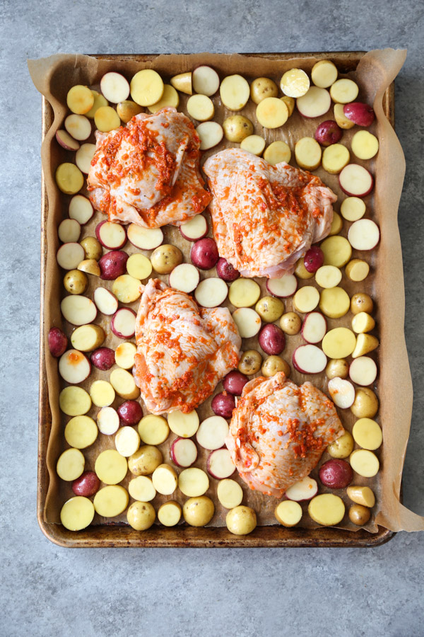 red pepper chicken covered in peri peri sauce on a sheet pan with potatoes