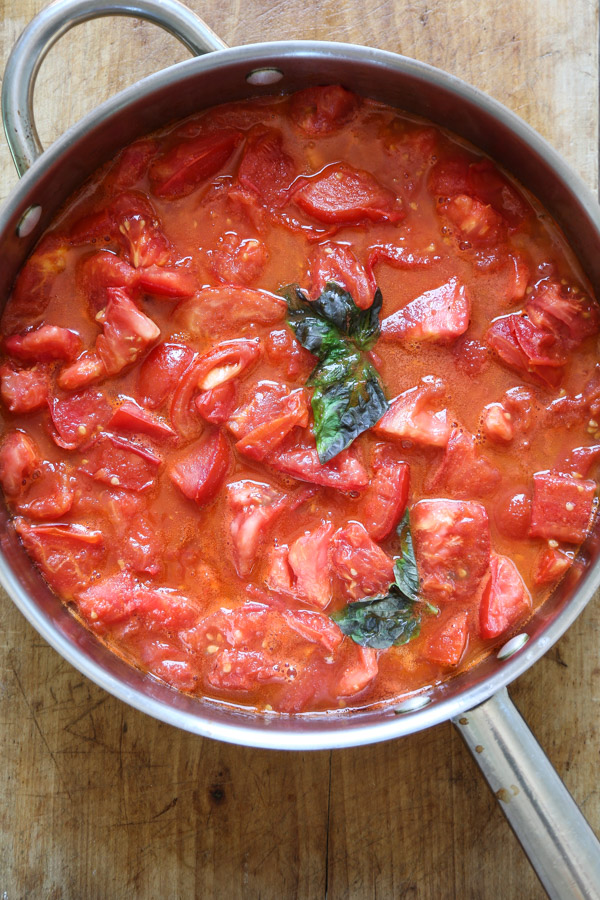 Saucepan of simmering fresh tomatoes and basil on a wood board