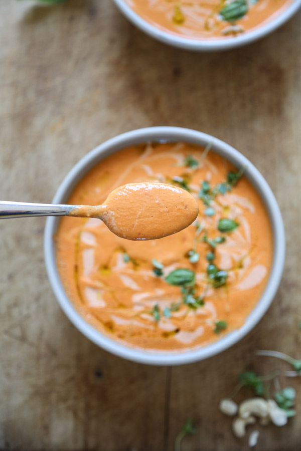 hand holding spoon of tomato basil soup on a board