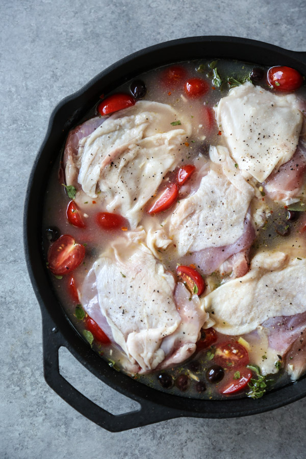 raw chicken in a skillet with tomatoes and olives