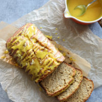 Lemon loaf cake on a board sliced with drizzle in a bowl