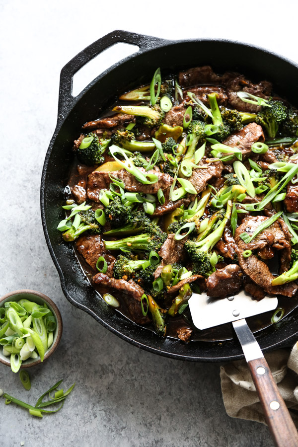 mongolian beef in a skillet with spatula and scallions