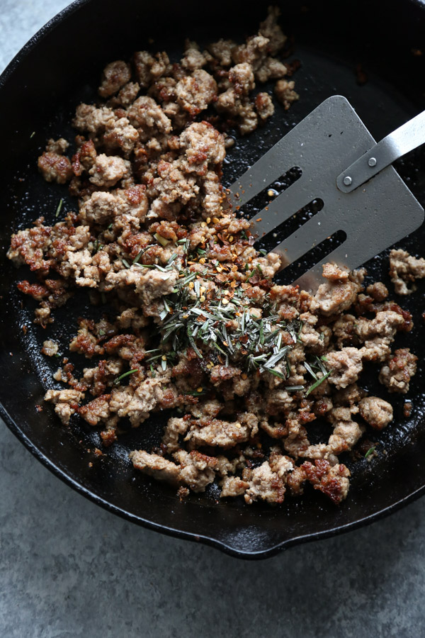 sausage in a cast iron skillet with spatula rosemary and chiles