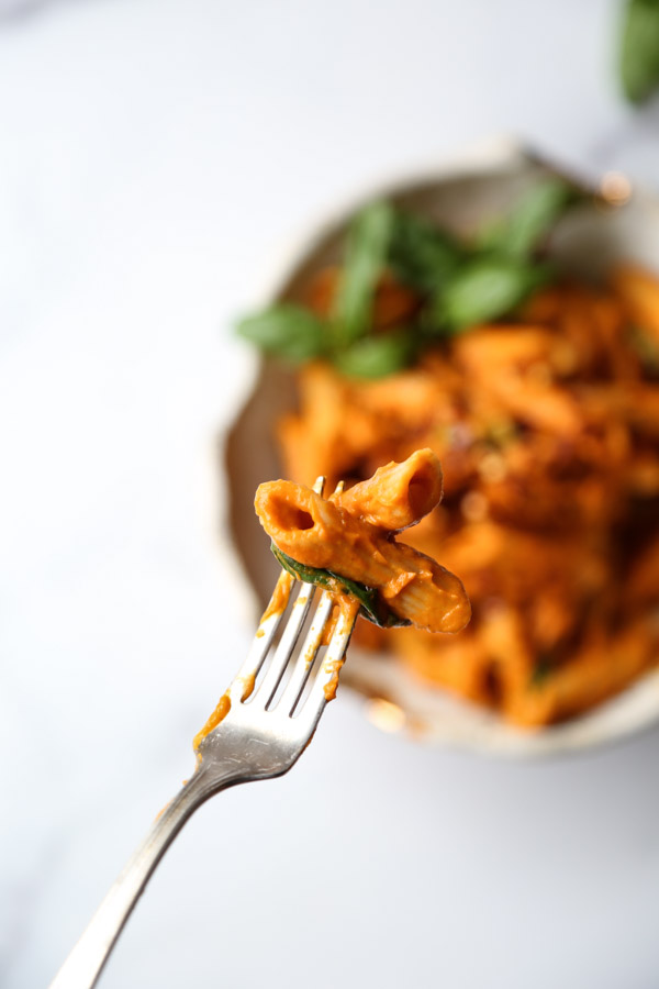 Gluten-Free penne covered low FODMAP pasta sauce in a bowl with fork and two penne in foreground