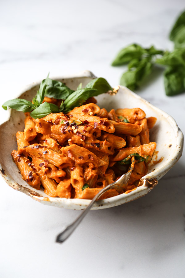 Gluten-Free penne with low FODMAP vodka sauce in a bowl with basil garnish and spoon