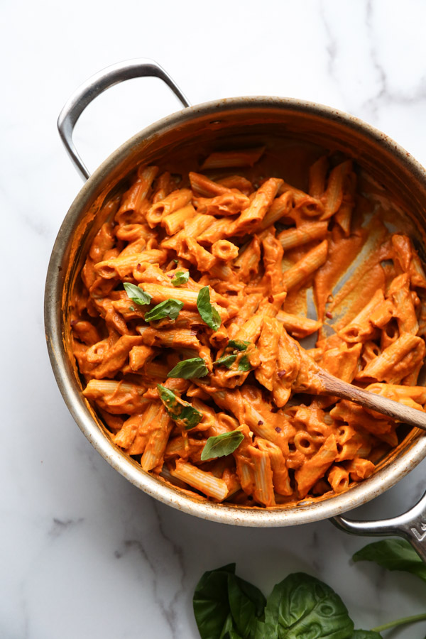 Gluten-Free penne in a skillet with low FODMAP vodka sauce, basil garnish and spoon