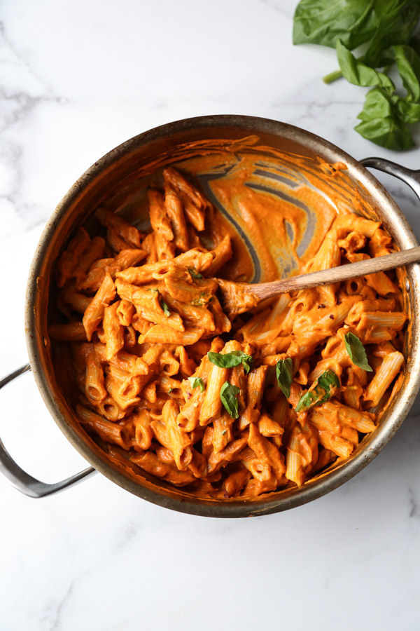 Gluten-Free penne in a skillet with low FODMAP vodka sauce, basil garnish mixed together
