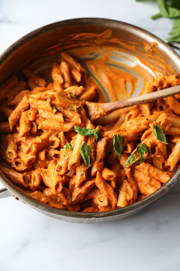 Gluten-Free penne with low FODMAP pasta sauce in a skillet with basil garnish and spoon