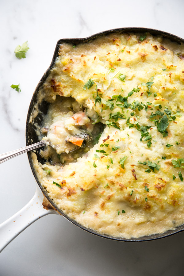 Overhead of gluten-free fish pie in a pan with a spoon in it and parsley garnish