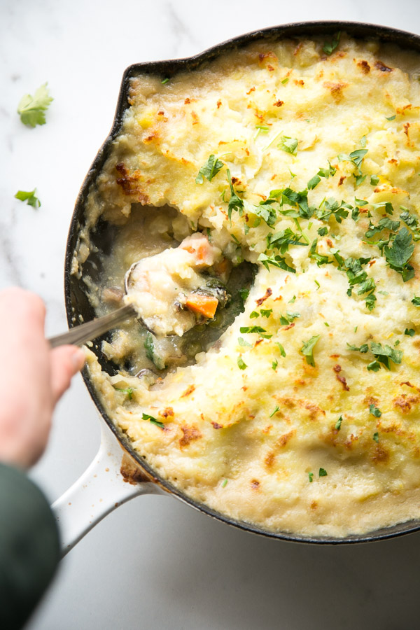 hand holding spoonful of dairy-free fish pie serving from the pan