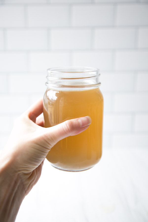 hand holding jar of Slow Cooker Gut-Healing Low FODMAP Chicken Broth for Soup