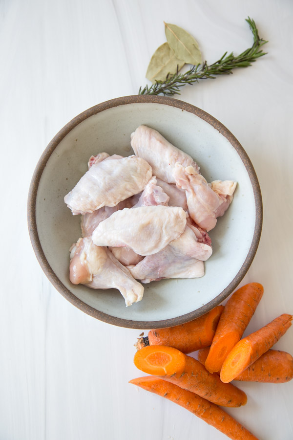 chicken wings in a bowl next to carrots and low fodmap herbs before going in the Slow Cooker 