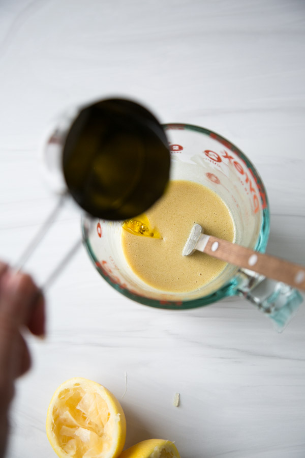 hand pouring olive oil into a cup measure of low fodmap dressing