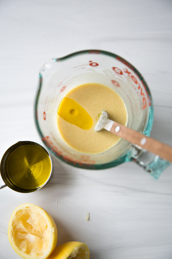 Cup of low-fodmap dressing with a slick of oil on top and lemons next to it
