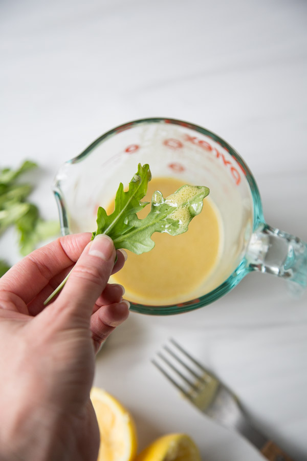 Hand holding a piece of arugula dipped in low fodmap dressing