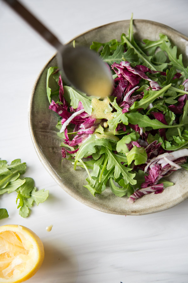Low fodmap lemon Dijon dressing on arugula and radicchio on a plate with a spoonful of dressing on the side