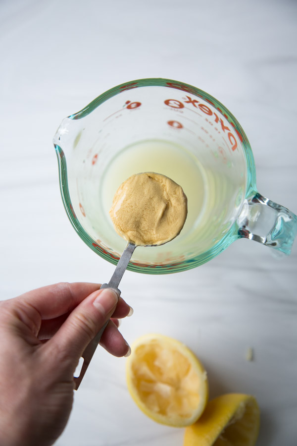 Dijon mustard held in a tablespoon over cup measure of lemon juice