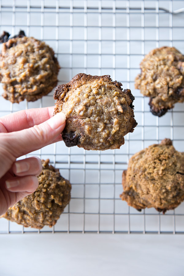 baked steel cut oat cookies with chocolate chunks on a wire rack with hand holding one