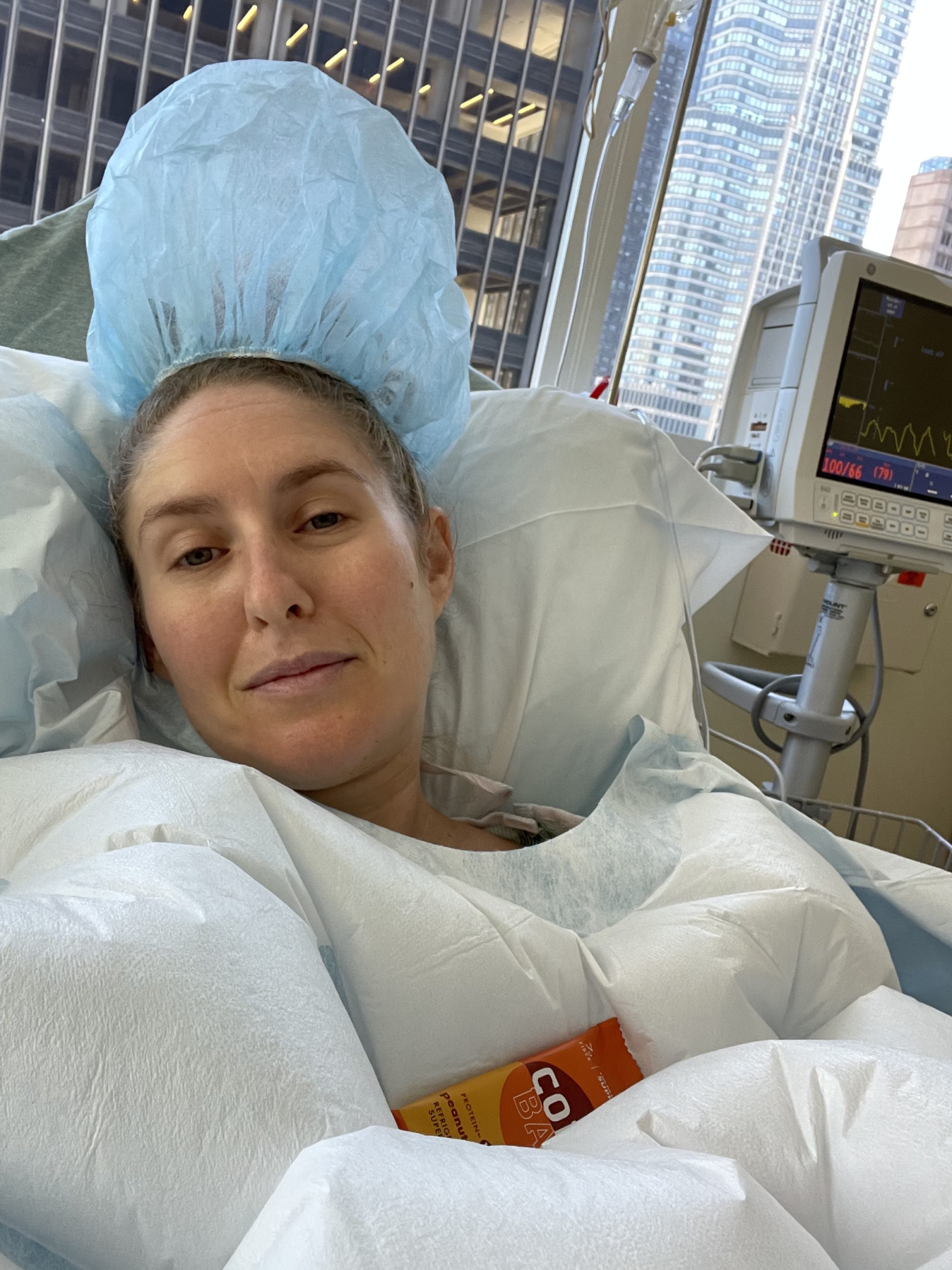 Woman in hospital gown and bonnet after egg retrieval recovering
