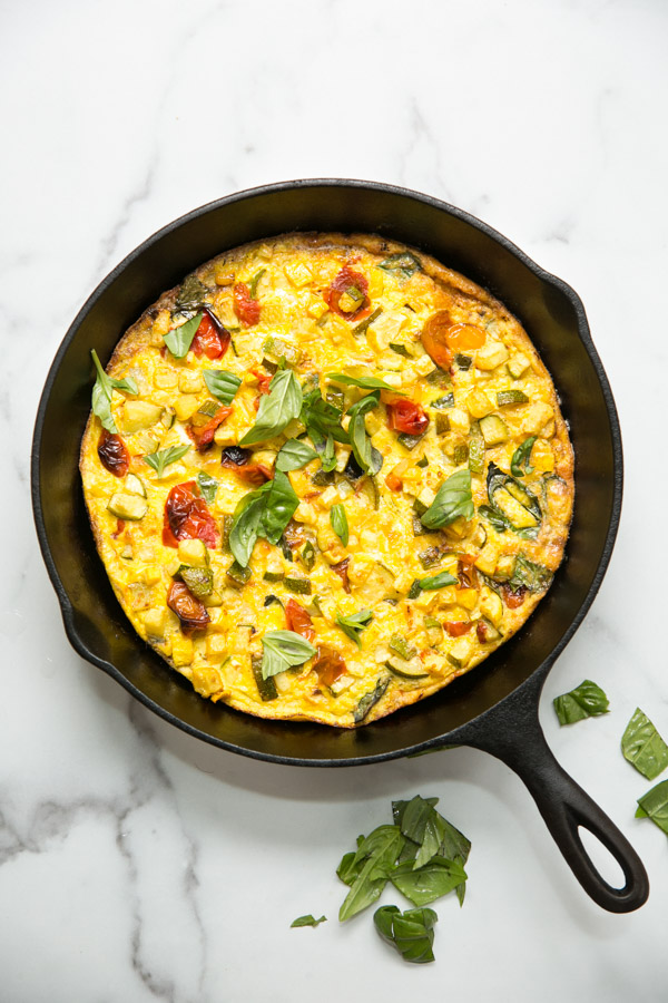 zucchini frittata in a skillet with basil leaves on the counter