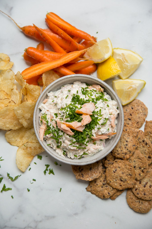 Smoked Salmon Spread in a bowl with crudites, crackers, potato chips and lemon wedges around it