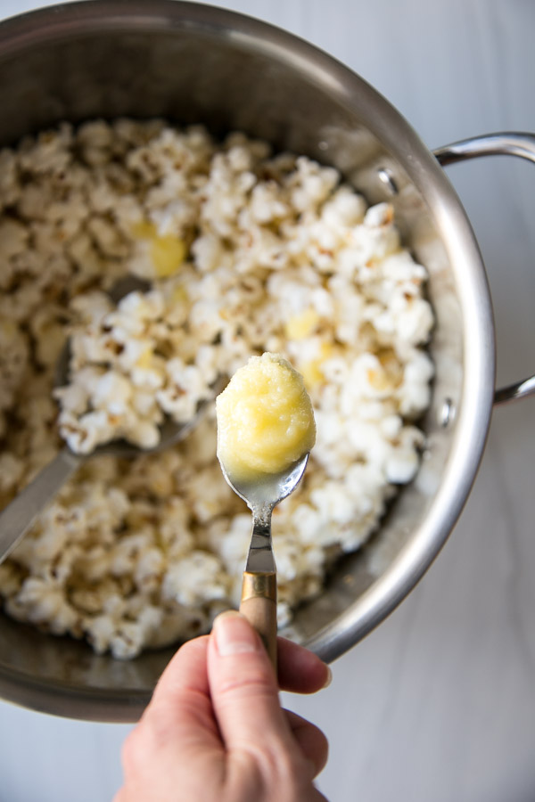 hand holding spoonful of butter over low fodmap popcorn in a pot