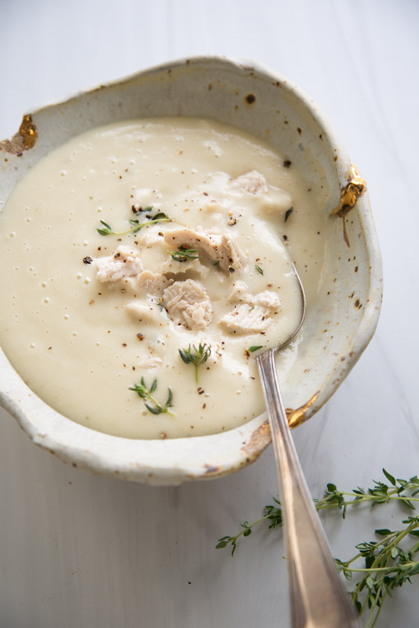 Bowl of gluten-free cream of chicken soup with thyme sprigs and spoon