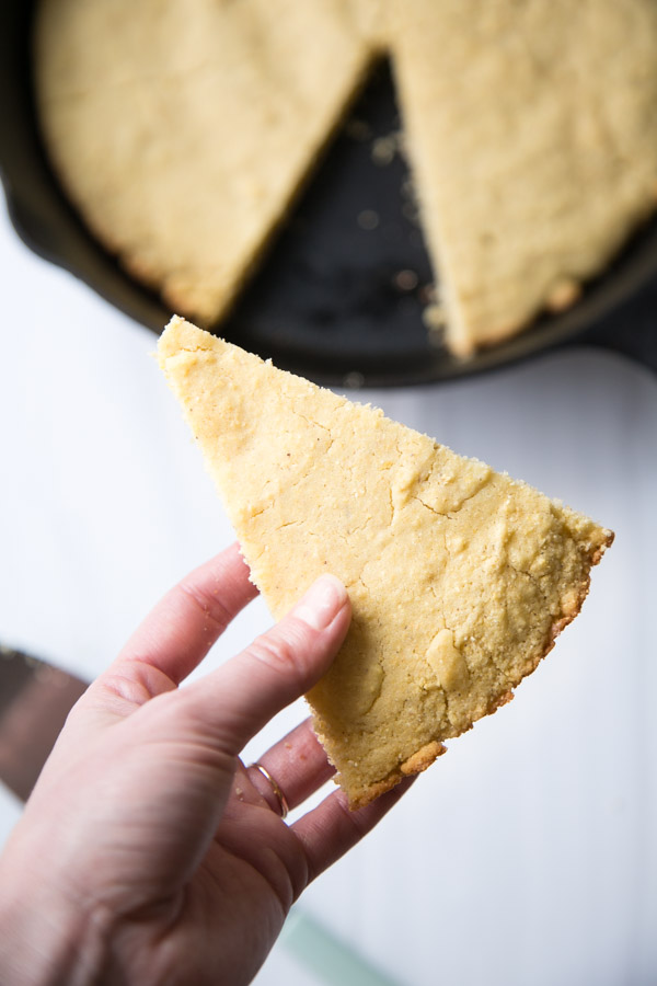 hand holding slice of gluten-free cornbread with skillet in the background