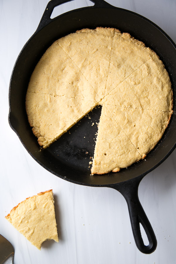 gluten-free cornbread in a skillet with one slice on marble counter