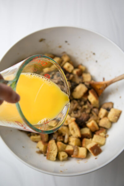cup measure of stock and eggs pouring into a mixing bowl over gluten-free cornbread