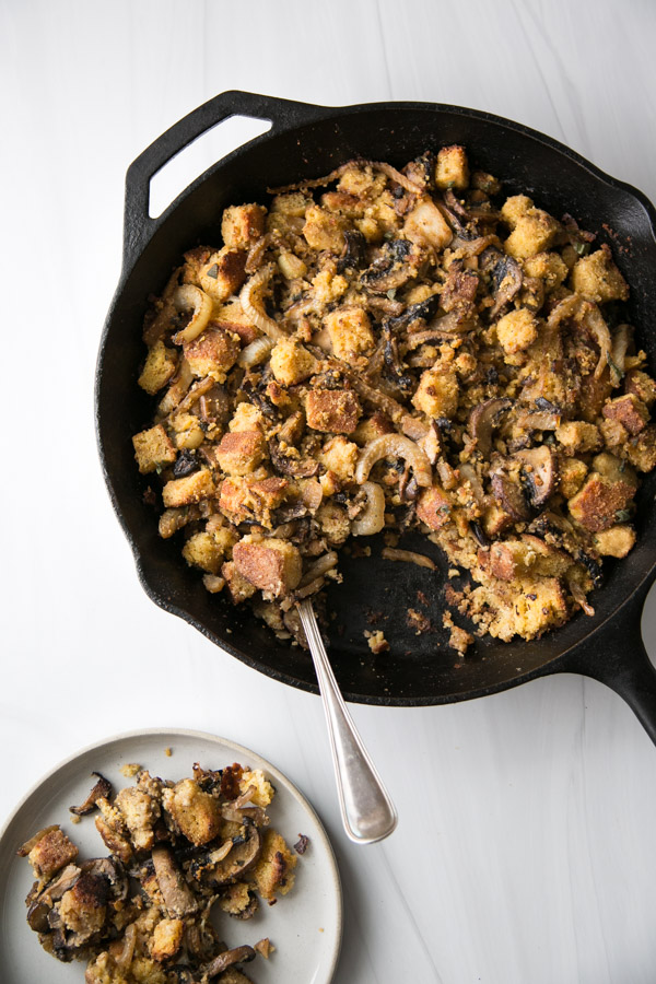 gluten-free cornbread stuffing in a skillet with spoon and plate full of dressing next to it