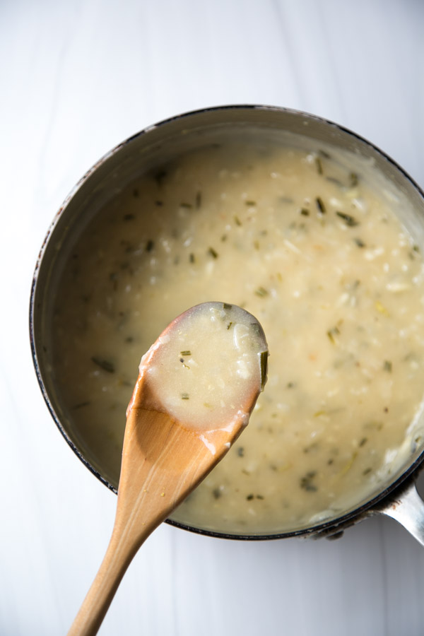 spoonful of gluten-free gravy with shallots and rosemary over the pan