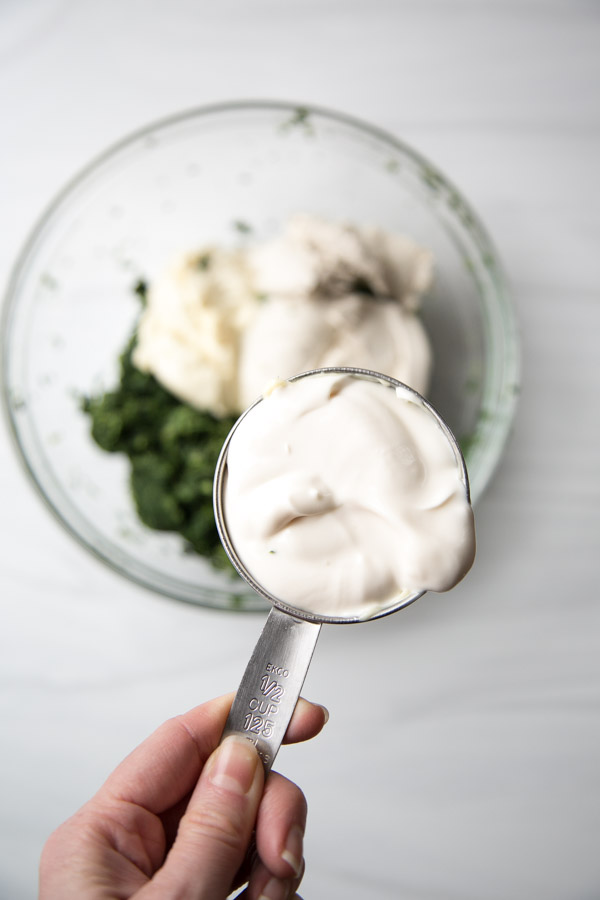 cup of dairy-free sour cream over bowl of spinach dip ingredients